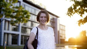 Junge Frau steht im Sonnenuntergang lächelnd vor dem Gebäude der HUK-COBURG