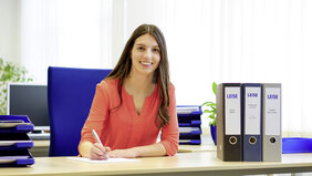 Lächelnde junge Frau mit roter Bluse arbeitet am Schreibtisch