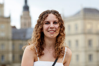 Junge Frau mit lockigen Haaren steht vor dem Schloss Ehrenburg in Coburg