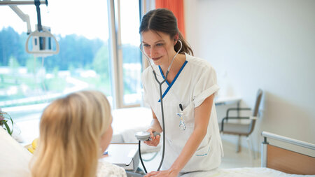 Junge Pflegekraft versorgt eine Patientin in einem Krankenhauszimmer