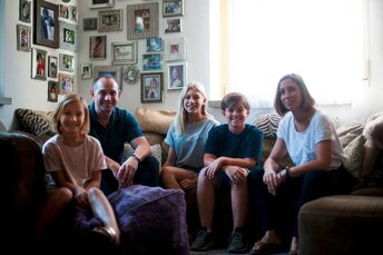 Junge Familie mit drei Kindern sitzt lächelnd auf einer Wohnzimmercouch