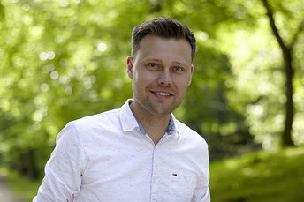 Junger Mann mit einem weißen Hemd steht lächelnd im Wald