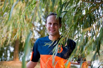 Junger lächelnder Mann in Fahrradbekleidung steht im Grünen