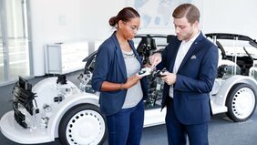 Mitarbeitende der Firma Brose stehen vor einem Auto und begutachten ein Bauteil