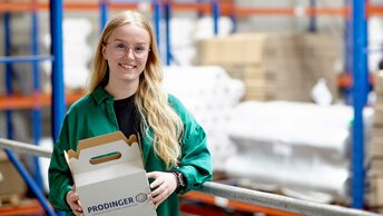 Junge Mitarbeiterin der Firma Prodinger steht mit Kartonage in einem Lager