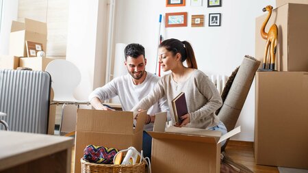 Junges Paar packt in einem hellen Zimmer Umzugskartons aus