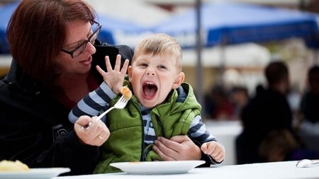 Frau füttert ein vergnügtes kleines Kind auf einem Volksfest