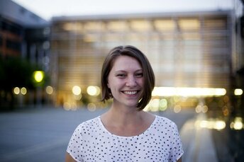 Junge Frau steht vor dem Gebäude der HUK-COBURG am Abend