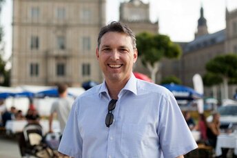 Lachender Mann in legerer Kleidung steht Schlossplatz in Coburg