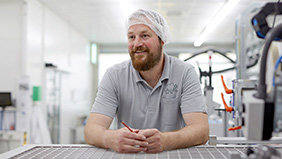 Bärtiger lächelnder Mann steht in Arbeitkleidung in einer Werkstatt